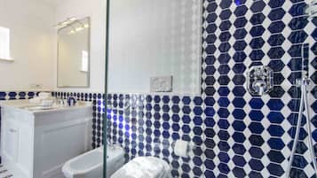 A bathroom with a white vanity, a large mirror, a shower with a glass door, and a blue and white hexagonal tile backsplash.