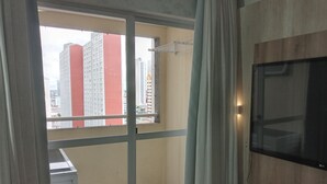 Un balcón con vistas a edificios altos, un televisor montado en la pared y una ventana con cortinas.