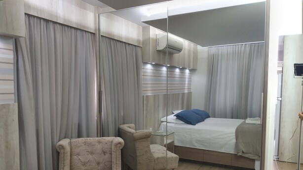 Una habitación de hotel moderna con un espejo grande, una cama con almohadillas azules, un sillón pequeño y una mesita de noche.