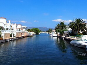Un canal bordé de bateaux et d’immeubles, avec des montagnes en arrière-plan.