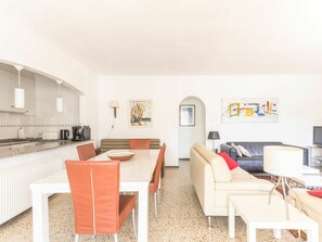 Un salon moderne comprenant un canapé, une table à manger avec des chaises, un coin cuisine avec une cuisinière et un téléviseur.