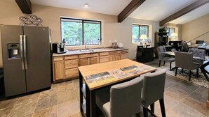 Una cocina moderna con refrigerador, pileta doble y armarios de madera. Hay una zona de comedor con mesa y sillas.