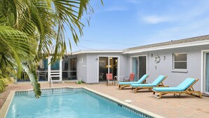Ein Swimmingpool mit Liegestühlen, eine überdachte Terrasse und ein Gebäude mit Tür und Fenstern.