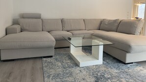 En moderne stue med en beige hjørnesofa, et glasbord og et mønstret gulvtæppe.