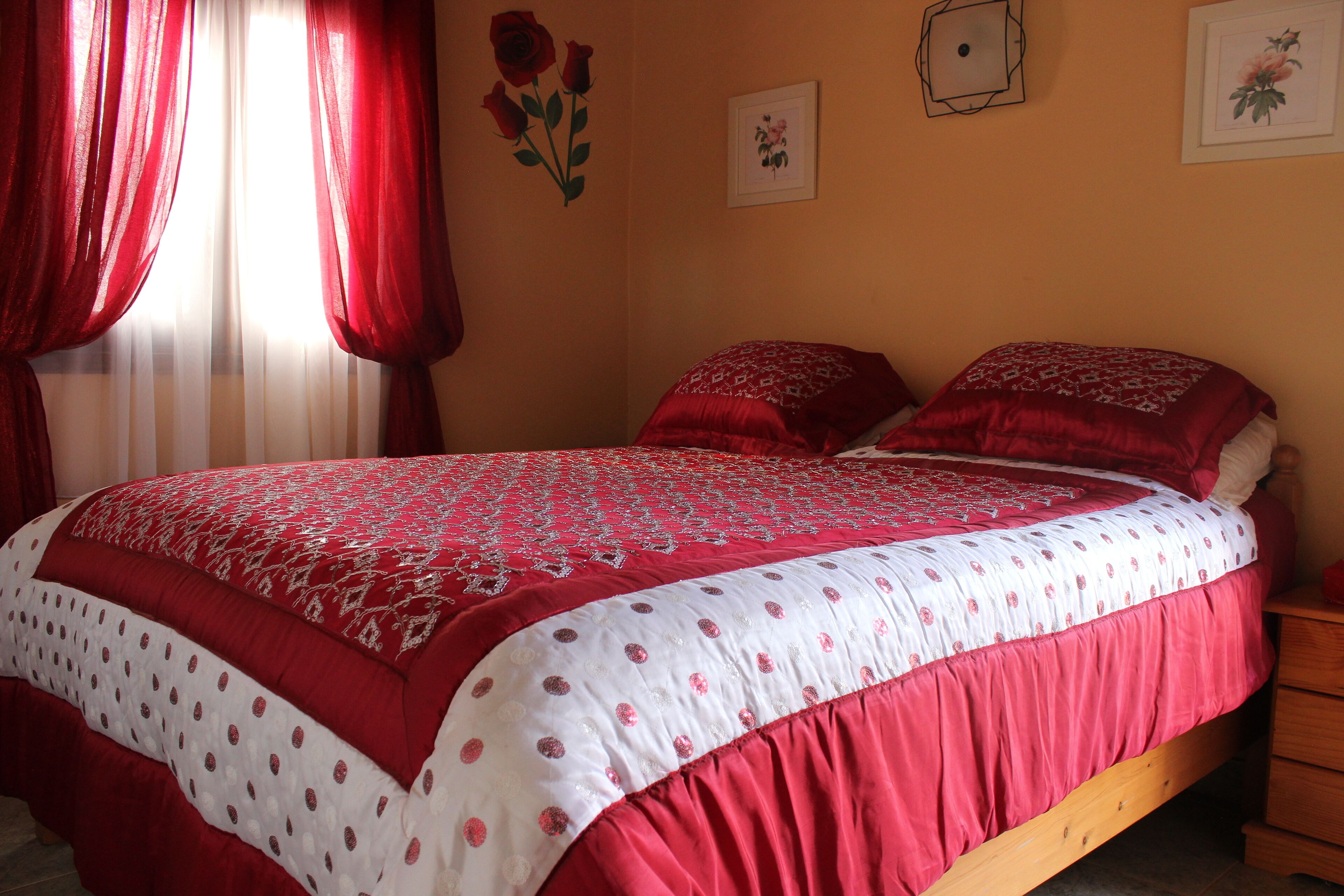 Een slaapkamer met een bed, rode gordijnen en wanddecoraties.