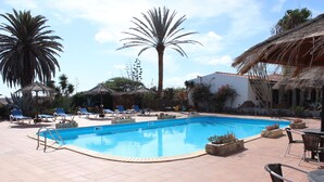 A swimming pool with lounge chairs and a thatched-roof structure. - Comfortable 1-Bed Bungalow in Parque Holandés (La Oliva)