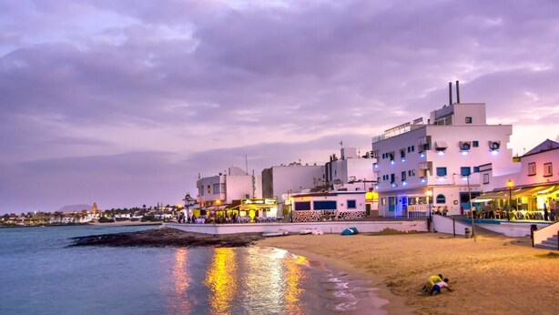 A coastal town with buildings along the waterfront, a sandy beach, and a pier in the distance. - Comfortable 1-Bed Bungalow in Parque Holandés (La Oliva)