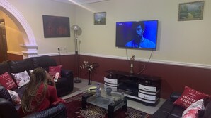 Ein Wohnzimmer mit einem an der Wand montierten Flachbildfernseher, einem Glastisch und zwei Sofas mit roten Kissen.