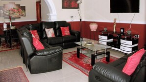 Ein Wohnzimmer mit einem schwarzen Ledersofa, einem Glastisch und einem an der Wand montierten Fernseher.