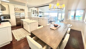 A modern kitchen with white cabinetry, a central island, and a dining area with a wooden table and chairs.