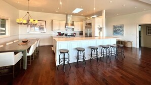 A spacious kitchen with a central island, bar stools, and a dining area with a long table.