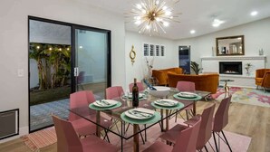 A modern dining area with a glass table, pink chairs, and a chandelier.