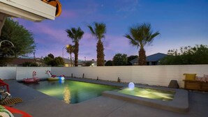 A backyard with a swimming pool, palm trees, and a flamingo float.