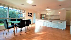 A modern kitchen with white cabinets, a stainless steel refrigerator, and a bar area with stools.