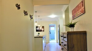 A narrow hallway with a wooden cabinet on the right, a kitchen area with a sink and cabinets in the center, and a door leading to an outdoor area.