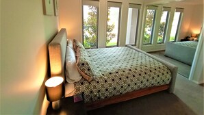 A bedroom with a bed, a bedside lamp, and a window with a view of trees.
