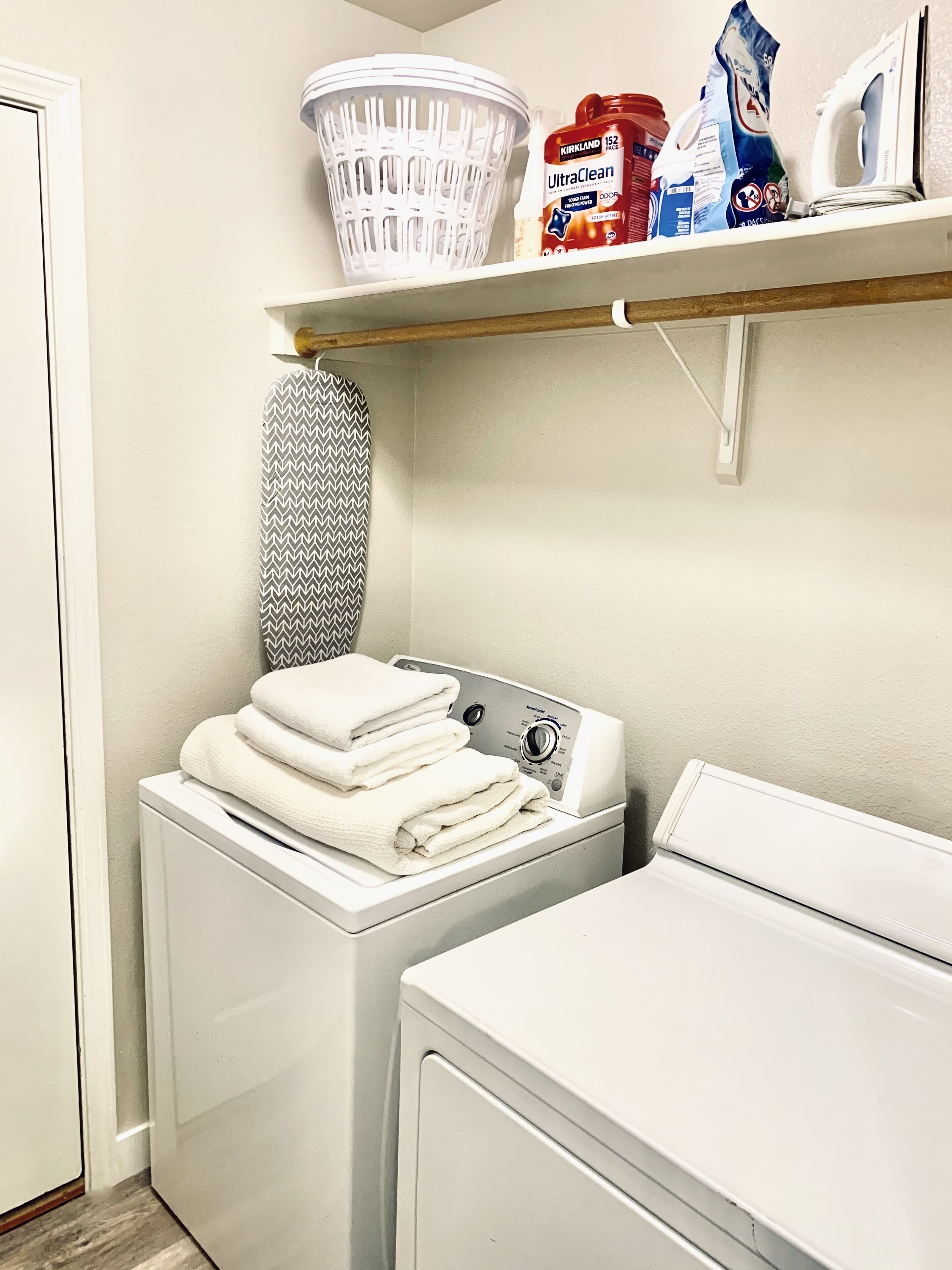 Un espace dédié à la buanderie, comprenant un lave-linge et un sèche-linge à chargement frontal, un panier et des produits de lessive rangés sur une étagère.