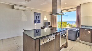 Una cocina moderna con una isla central, horno integrado y un amplio ventanal con vistas al mar.