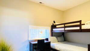 A small room with a bunk bed, a desk with a chair, and a potted plant.