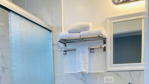 A bathroom with a glass shower enclosure, a toilet, a sink with a mirror, and a towel rack with towels.