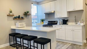 A modern kitchen with white cabinets, a central island with bar stools, a stove, a microwave, and a coffee maker.