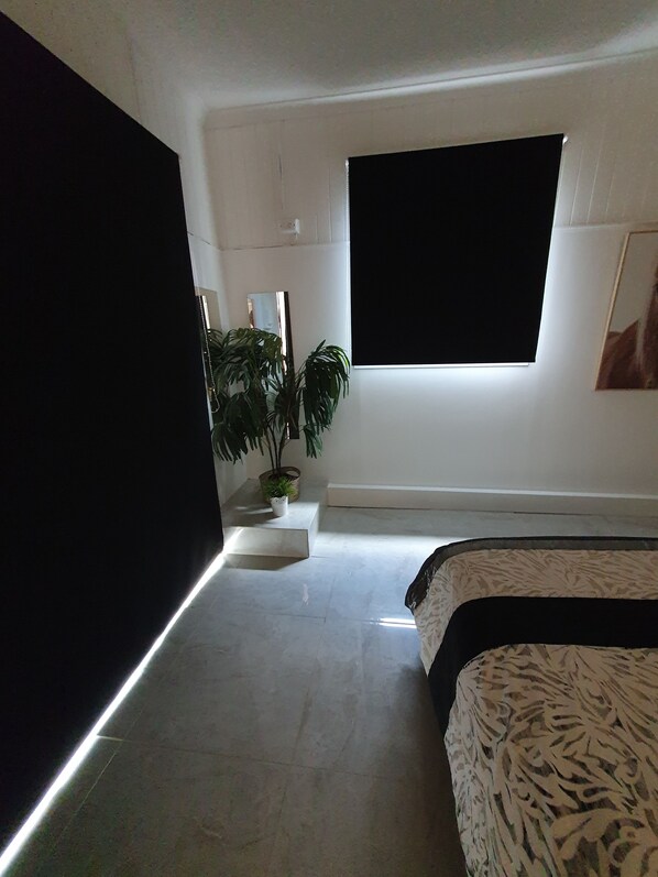 Un dormitorio moderno con un ventanal grande, una planta en maceta y una cama con ropa de cama estampada.