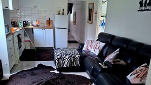 A living room with a black leather sofa, a zebra-patterned ottoman, and a black and white rug. - Farm Stay Cottage in the beautiful Gold coast hinterland (Illinbah)