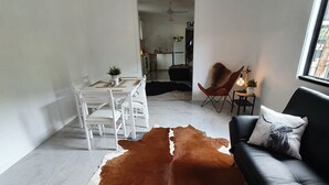 A modern living room with a cowhide rug, a black sofa with a decorative pillow, a dining table with chairs, and a ceiling fan. - Farm Stay Cottage in the beautiful Gold coast hinterland (Illinbah)