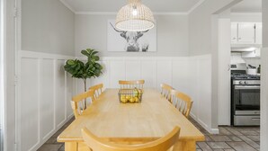 Une salle à manger avec une table en bois, des chaises, un luminaire suspendu et un tableau accroché au mur.