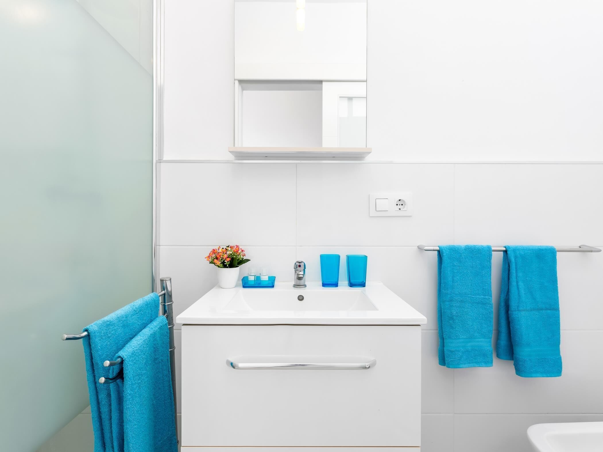 A modern bathroom with a white sink, a mirror above it, and two blue towels hanging on a towel rack.