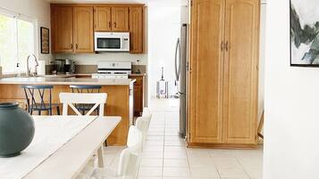 A modern kitchen with wooden cabinets, a dining area with a white table and chairs, and a large rug leading to a door.