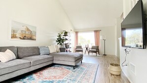 A modern living room with a sectional sofa, a large flat-screen TV, a patterned rug, and a bookshelf. - The perfect stay for Families and Friends (Oceanside)
