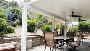 A covered patio with a table and chairs, surrounded by a garden with various plants and a stone wall. - The perfect stay for Families and Friends (Oceanside)