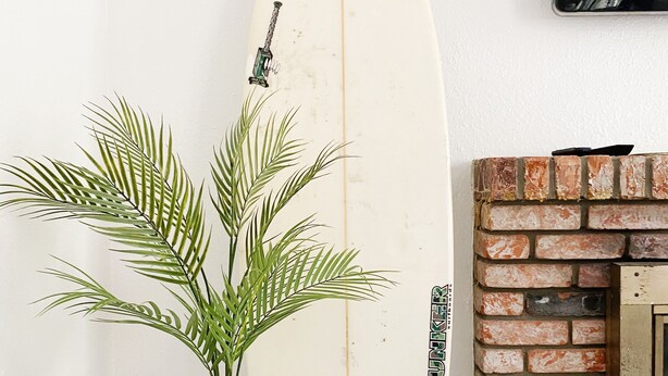 A surfboard leaning against a white wall, a potted plant on a small table, and a brick fireplace. - The perfect stay for Families and Friends (Oceanside)