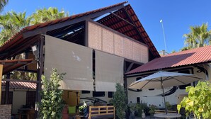 A covered outdoor area with a dining table and benches, surrounded by potted plants and a gravel ground. - Spacious Palapa half a block of waterfront. (Loreto)