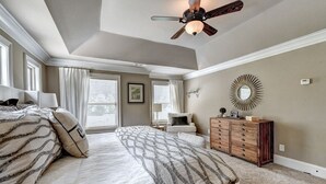 A bedroom with a large bed, a ceiling fan, a dresser, and a wall-mounted mirror. - 9-bedroom Luxury Home, 4.8 Acre w/ Pool, Minutes to Suwanee downtown and Lake (Suwanee)