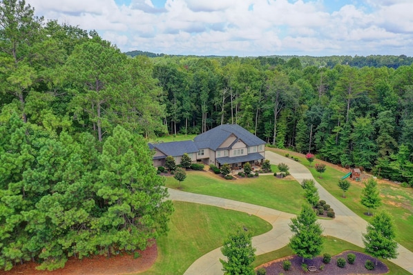 A two-story house with a dark roof, surrounded by a well-maintained lawn and a winding driveway.