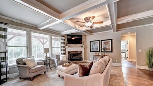A spacious living room with a fireplace, a ceiling fan, and large windows. - 9-bedroom Luxury Home, 4.8 Acre w/ Pool, Minutes to Suwanee downtown and Lake (Suwanee)
