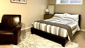 Une chambre à coucher avec un lit, une chaise, une table de chevet, une lampe, un miroir et une fenêtre.