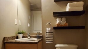 Une salle de bain avec un meuble-lavabo en bois, des toilettes blanches et des étagères où sont rangées les serviettes.