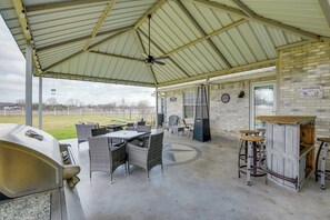 Un espace extérieur aménagé en terrasse, avec un barbecue, des meubles en osier, un bar avec des tabourets et un jeu de fléchettes.