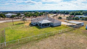 A large house with a spacious backyard, a fenced area, and a distant view of other buildings and trees. - 'Leaping Toad Ranch' ~ 9 Mi to Lake Granbury! (Granbury)