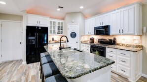 A modern kitchen with white cabinetry, a black refrigerator, a granite countertop, and a built-in oven. - 'Leaping Toad Ranch' ~ 9 Mi to Lake Granbury! (Granbury)