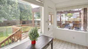 Habitación con vista a un patio trasero, una terraza de madera y una planta en maceta sobre una mesa.
