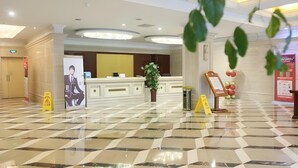 A hotel lobby with a reception desk, a large poster, a potted plant, and a check-in counter.