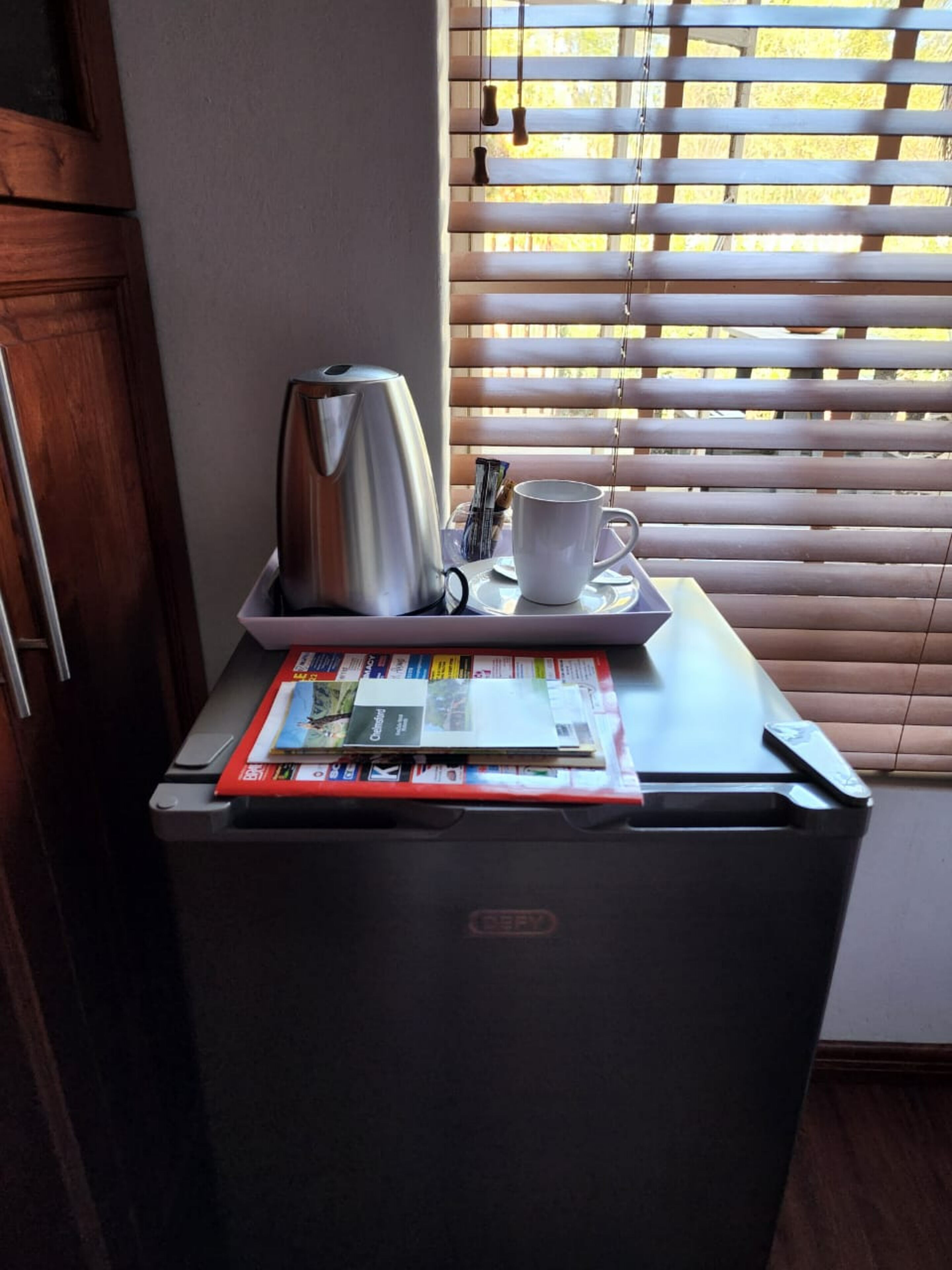 A compact kitchenette with a coffee maker, a mug, and a magazine on a small table.