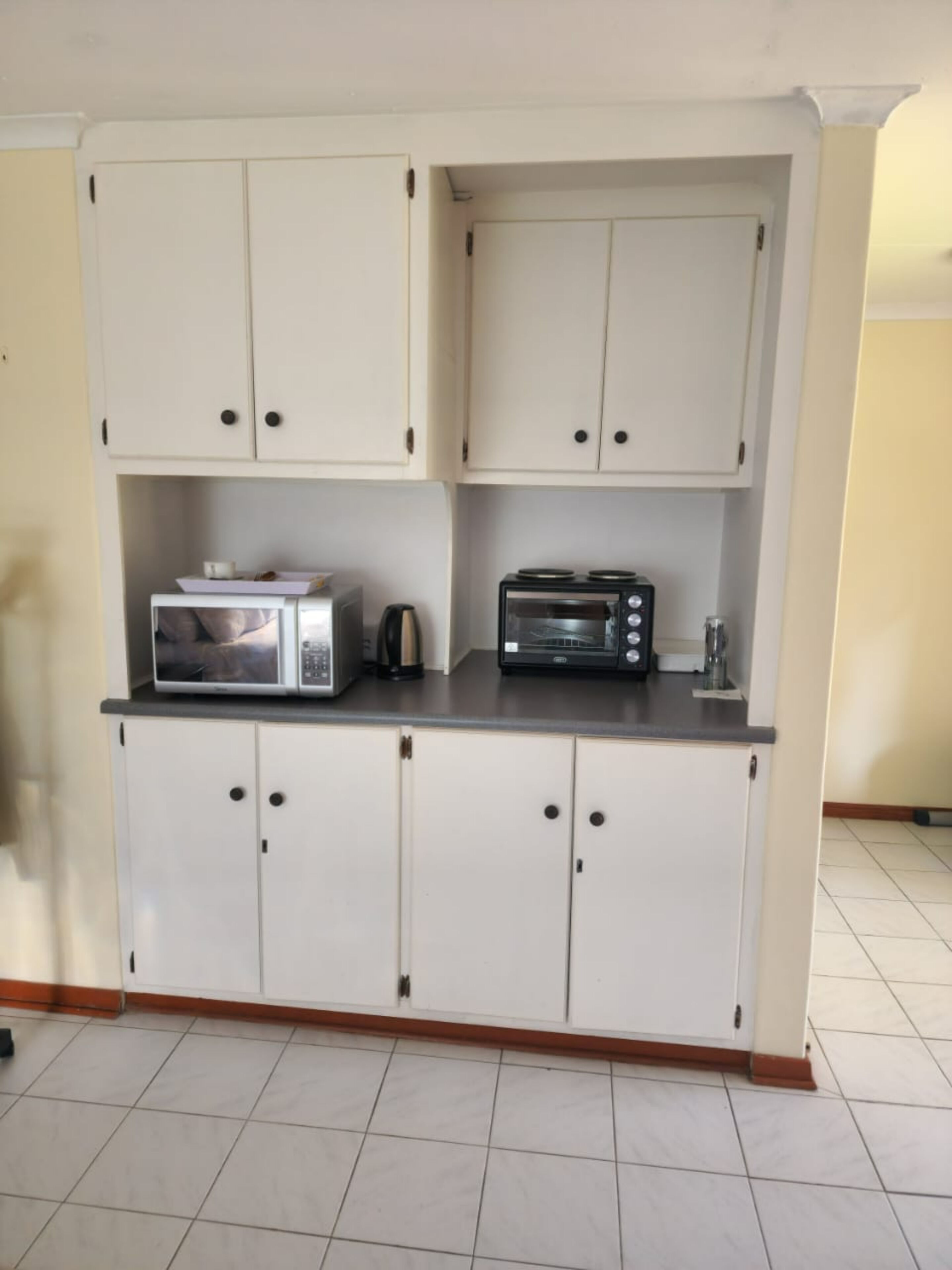 Una cocina con gabinetes blancos, microondas, tostadora y cafetera.
