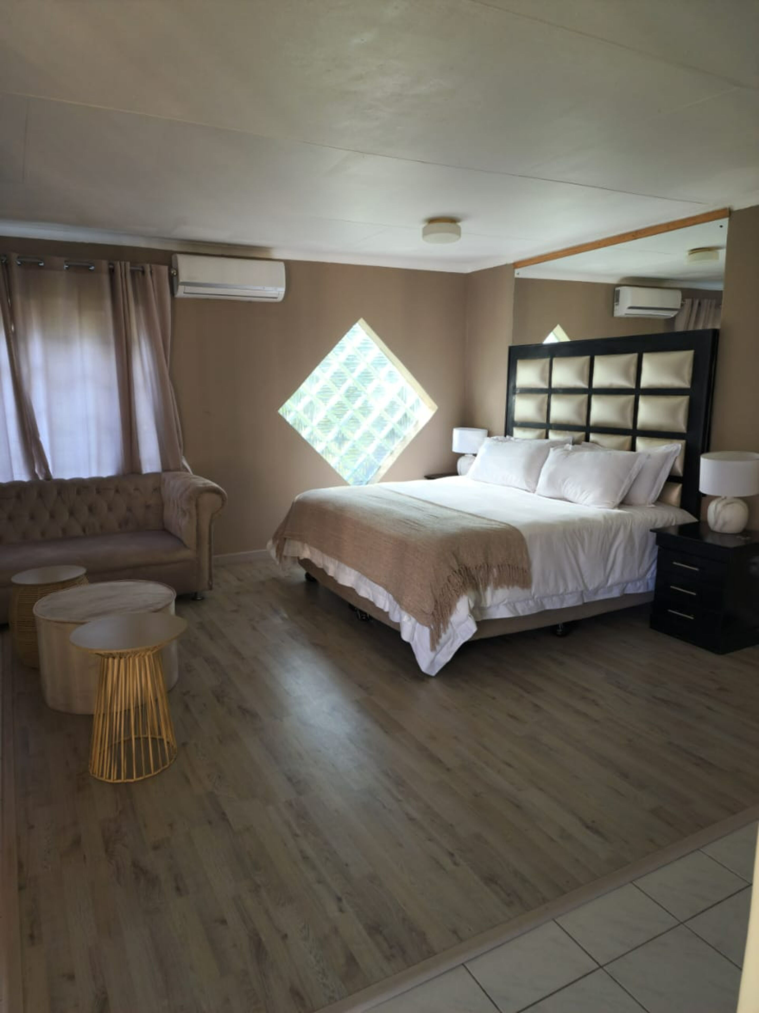 A bedroom with a bed, a sofa, a window, and a mirror.
