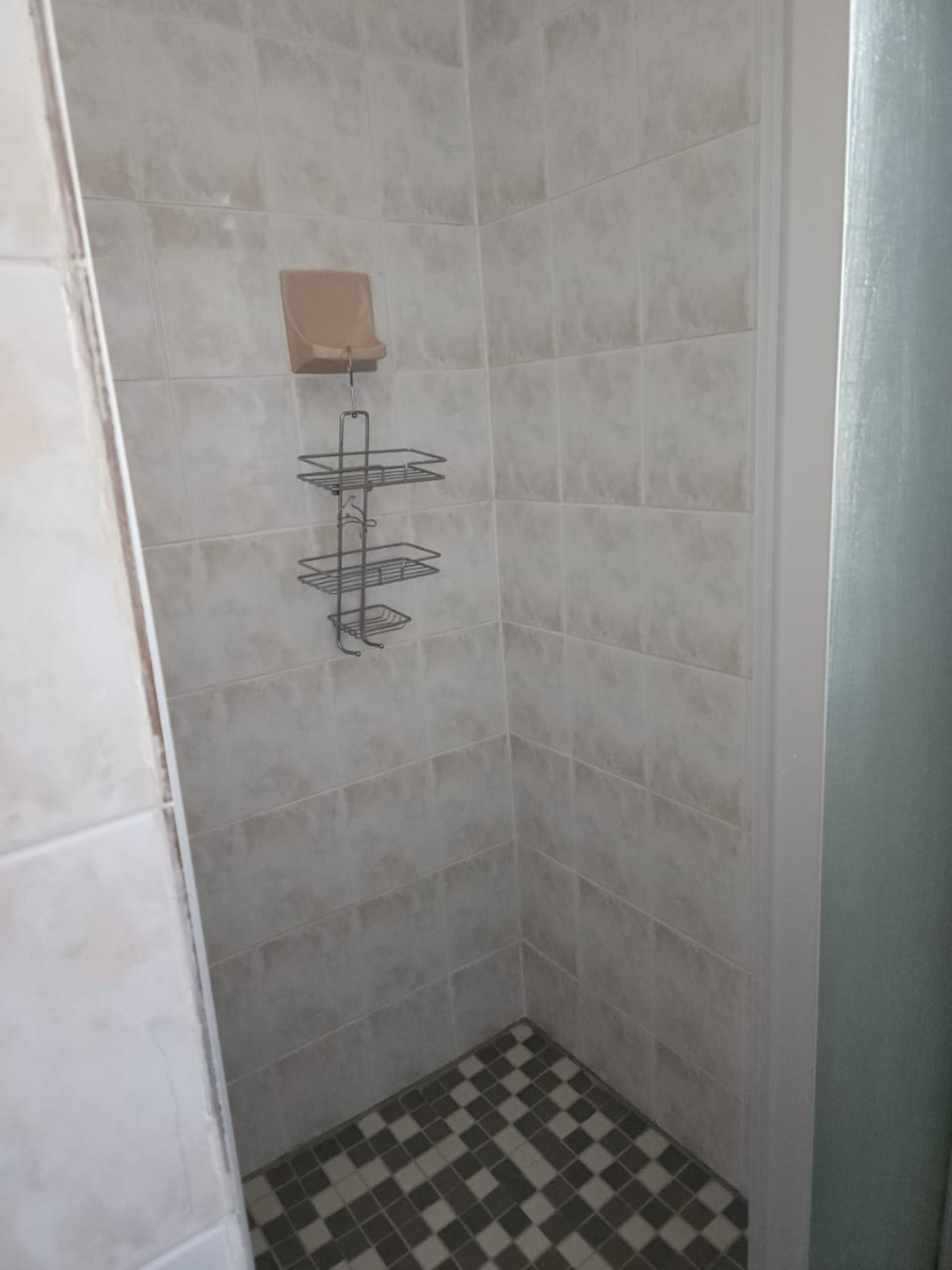 A corner shower with grey tiles and a checkered floor.