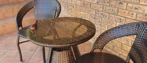 A patio area with two wicker chairs and a glass table, set against a brick wall.